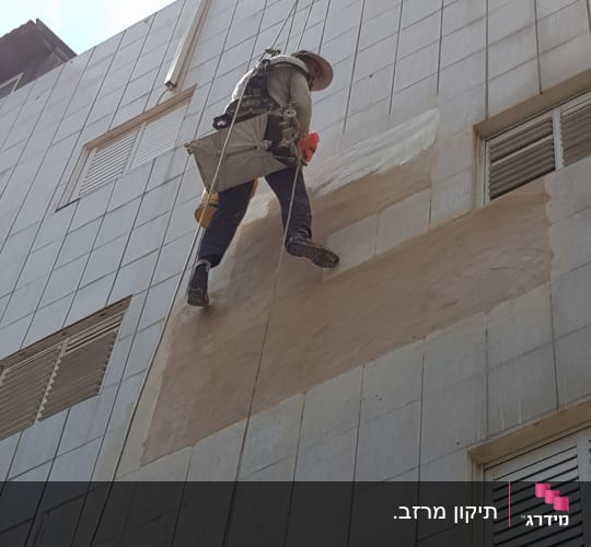 אדם על חבלים צובע קיר חיצוני של בניין